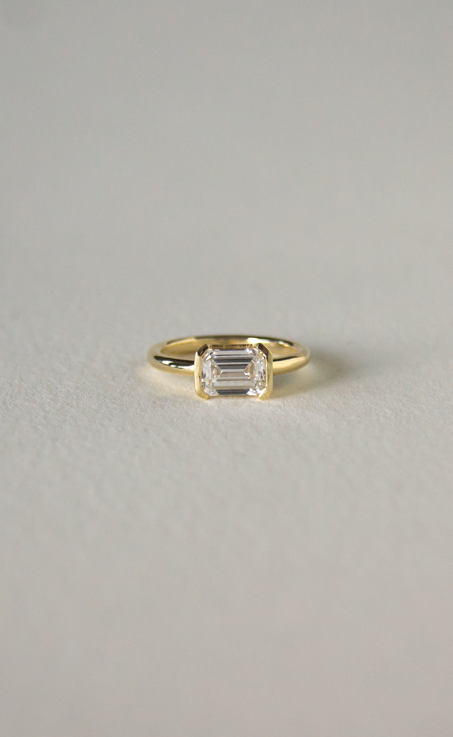 East–West Emerald Ring featuring a horizontally set lab-grown emerald-cut diamond in a modern half-bezel 18K yellow gold design
